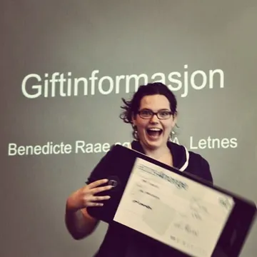 A young Queen Raae laughing and holding a giant cheque in front of a slide reading Giftinformasjon
