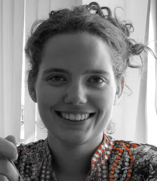 Black and white portrait of Queen Raae smiling, with orange embroidery on her top
